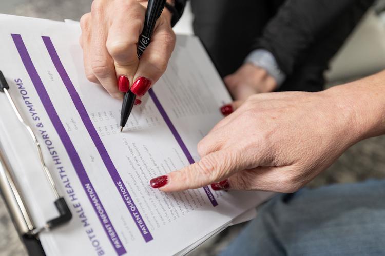 A close-up of the hands of a patient at ThrIVe Wheeling, filling out a patient form attached to a clipboard for a treatment to balance hormones in St. Clairsville and Wheeling. The form asks about the patient's medical history and symptoms.